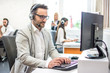 © Bojan - Call centre agent with headset working on computer in customer support helpdesk office