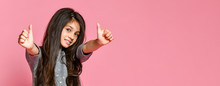 Portrait Of A Pretty Attractive Little Girl In A Dark Dress, Showing Thumbs Up With Two Hands On A Pink Background