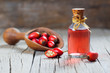 Glass bottle of rosehip seed essential oil with fresh rose hip fruits in shovel on wooden rustic background. Dogrose oil with fresh dog roses