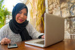 © TheVisualsYouNeed - middle age Asian Indonesian Muslim woman in traditional hijab head scarf working relaxed at home garden running online business in internet job success