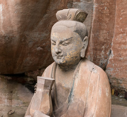 Statue of disciple or follower holding a bowl with two hands in front of giant Buddha at Dazu Rock Carvings at Mount Baoding or Baodingshan in Dazu, Chongqing, China. UNESCO World Heritage Site.