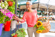 © Dragana Gordic - Attractive mature woman shopping in an outdoors fresh flowers market stall, buying and picking from a large variety of colorful floral bouquets during a sunny day in the city.