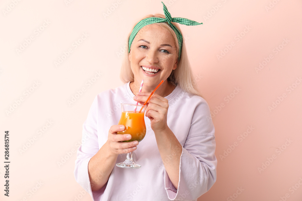 Happy mature woman with fresh cocktail on light background
