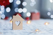 Wooden icon of house with hole in form of heart with red home Christmas decor and blurred bokeh background in daylight.