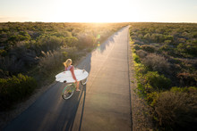 Beautiful Blonde Surfer Girl On Her Way To The Beach On Her Bicycle With Her Surfboard.