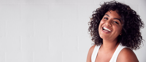 portrait of smiling casually dressed woman in vest top standing against white brick studio wall