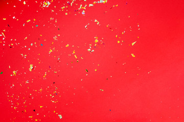 Wall Mural - Red background on which a lot of multi-colored clapperboard foil and stars confetti, holiday concept.  Christmas card.  Place for text. Flat lay.