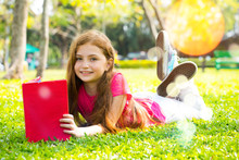 Cute Little Blond Girl Reading Book Outside On Grass