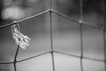 Closeup torn old rope net from a football goal with a dry thread end and knots and a blurred background.