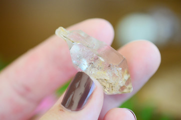 Wall Mural - Clear quartz point on wood table in natural lighting. Woman's hand - High Quality Clear Quartz healing stone, One of a Kind Quartz Point, great for a reiki healing! Unique formations, Quartz Scepter.