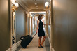 © davit85 - Young woman with handbag and suitcase in an elegant suit walks the hotel corridor to her room.