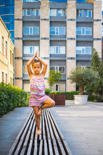 Little Girl Makes Yoga In Modern City.  Stands On One Foot. 