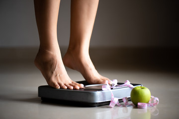 Wall Mural - Female leg stepping on weigh scales with measuring tape and green apple. Healthy lifestyle, food and sport concept.