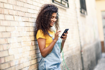 Wall Mural - Young North African woman texting with her smart phone outdoors