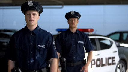 Wall Mural - Brave male officers standing against squad car on background, important job