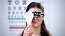 Woman In Phoropter Closing One Eye And Smiling, Choosing Correct Lens Diopter