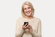 © fizkes - Smiling senior woman isolated in studio texting using smartphone