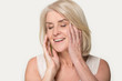 © fizkes - Smiling senior woman touch healthy face skin after beauty procedure