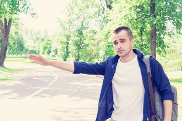 Traveler is on the side of the road, man try stop car, the concept of hitchhiking