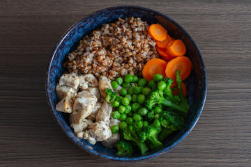 Wall Mural - boiled buckwheat with vegetables and chicken in a blue clay cup on table