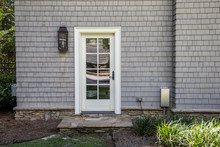 Cape Cod Style Home With White Wood Door At Back Entrance. Door Has Many Glass Windows And Outside Is An Exterior Light