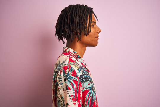 Afro man with dreadlocks on vacation wearing floral shirt over isolated pink background looking to side, relax profile pose with natural face with confident smile.