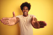 © Krakenimages.com - American man with afro hair wearing striped t-shirt standing over isolated yellow background looking at the camera smiling with open arms for hug. Cheerful expression embracing happiness.
