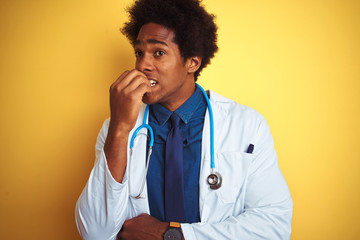 Poster - African american doctor man wearing stethoscope standing over isolated yellow background looking stressed and nervous with hands on mouth biting nails. Anxiety problem.