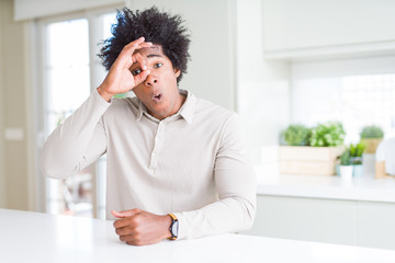 Poster - African American man at home doing ok gesture shocked with surprised face, eye looking through fingers. Unbelieving expression.