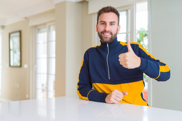 Wall Mural - Handsome man at home doing happy thumbs up gesture with hand. Approving expression looking at the camera with showing success.