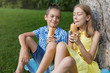 © aneduard - teens boy and girl sit on a lawn by a tree, eat a hot dog, talking, boy smiles