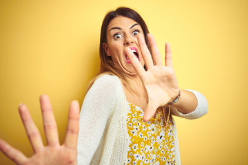 Canvas Print - Young beautiful woman wearing jacket standing over yellow isolated background afraid and terrified with fear expression stop gesture with hands, shouting in shock. Panic concept.