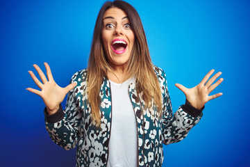 Wall Mural - Young beautiful woman wearing a jacket standing over blue isolated background celebrating crazy and amazed for success with arms raised and open eyes screaming excited. Winner concept