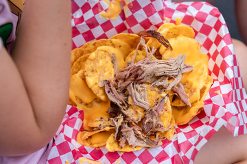 Pork meat nachos with cheese in girls lap, at a fair