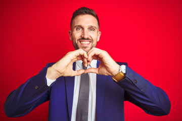 Young handsome business man over red isolated background smiling in love showing heart symbol and shape with hands. Romantic concept.