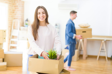 Poster - Beautiful young couple smiling in love holding cardboard boxes, happy for moving to a new home