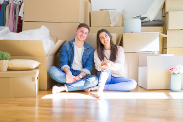 Poster - Young beautiful couple relaxing sitting on the floor around cardboard boxes at home, smiling happy moving to a new house