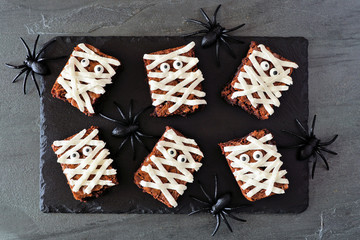 Wall Mural - Halloween mummy brownies, top view with spiders on a slate serving board on a dark stone background