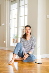 Wall Mural - Young beautiful woman sitting on the floor at home with serious expression on face. Simple and natural looking at the camera.