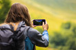 © Андрей Репетий - Young woman with backpack and mobile phone standing in the valley and taking a photo of a beautiful landscape in the mountains.