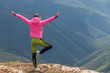 © Андрей Репетий - A young girl in pink coat with a raised hands doing yoga in mountains.