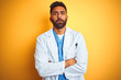 © Krakenimages.com - Young indian doctor man standing over isolated yellow background skeptic and nervous, disapproving expression on face with crossed arms. Negative person.
