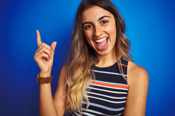 Canvas Print - Young beautiful woman wearing stripes t-shirt over blue isolated background very happy pointing with hand and finger to the side