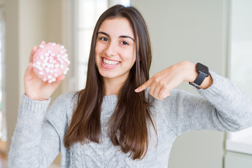 Sticker - Beautiful young woman eating sugar marshmallow pink donut with surprise face pointing finger to himself