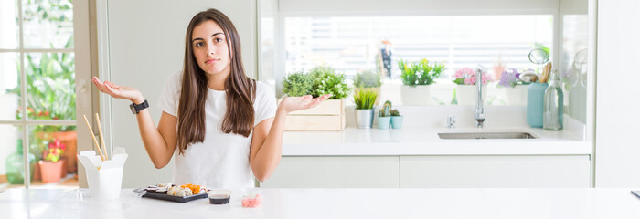 Poster - Wide angle picture of beautiful young woman eating asian sushi from delivery clueless and confused expression with arms and hands raised. Doubt concept.