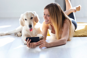 Sticker - Pretty young woman with her dog using mobile phone while lying on the floor at home.