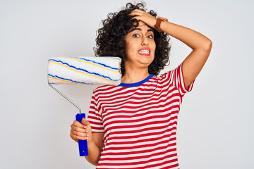 Sticker - Young arab painter woman with curly hair holding paint roller over isolated white background stressed with hand on head, shocked with shame and surprise face, angry and frustrated. Fear and upset 