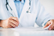© baranq - Close up of doctor reading and signing files and paperwork of patient