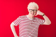 © Krakenimages.com - Young albino blond man wearing striped t-shirt and glasses over isolated red background smiling doing phone gesture with hand and fingers like talking on the telephone. Communicating concepts.