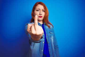 Canvas Print - Young beautiful redhead woman wearing denim shirt standing over blue isolated background Showing middle finger, impolite and rude fuck off expression